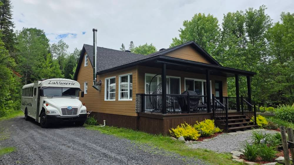 Skoolie staionné près d'un chalet en lambris de bois en forêt